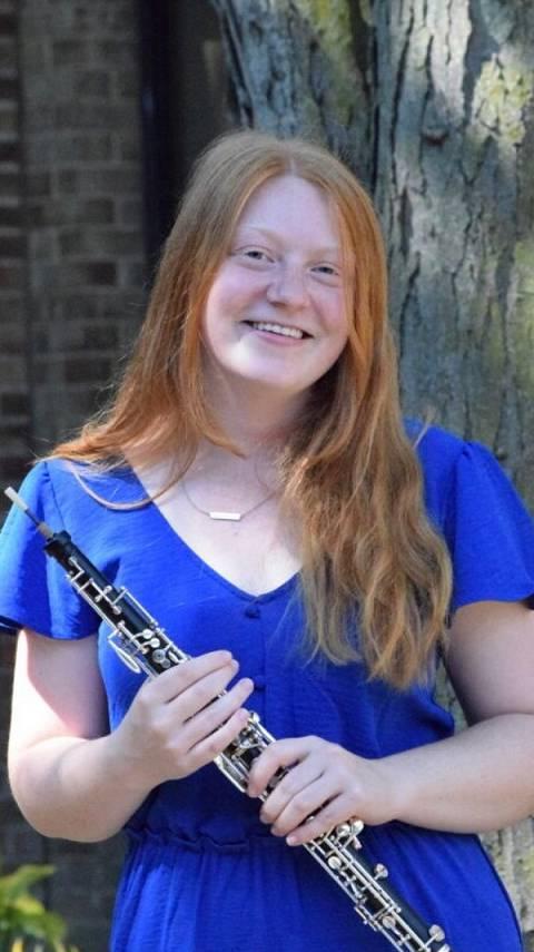 A photo of Joy Anderson, standing and holding her oboe outside.